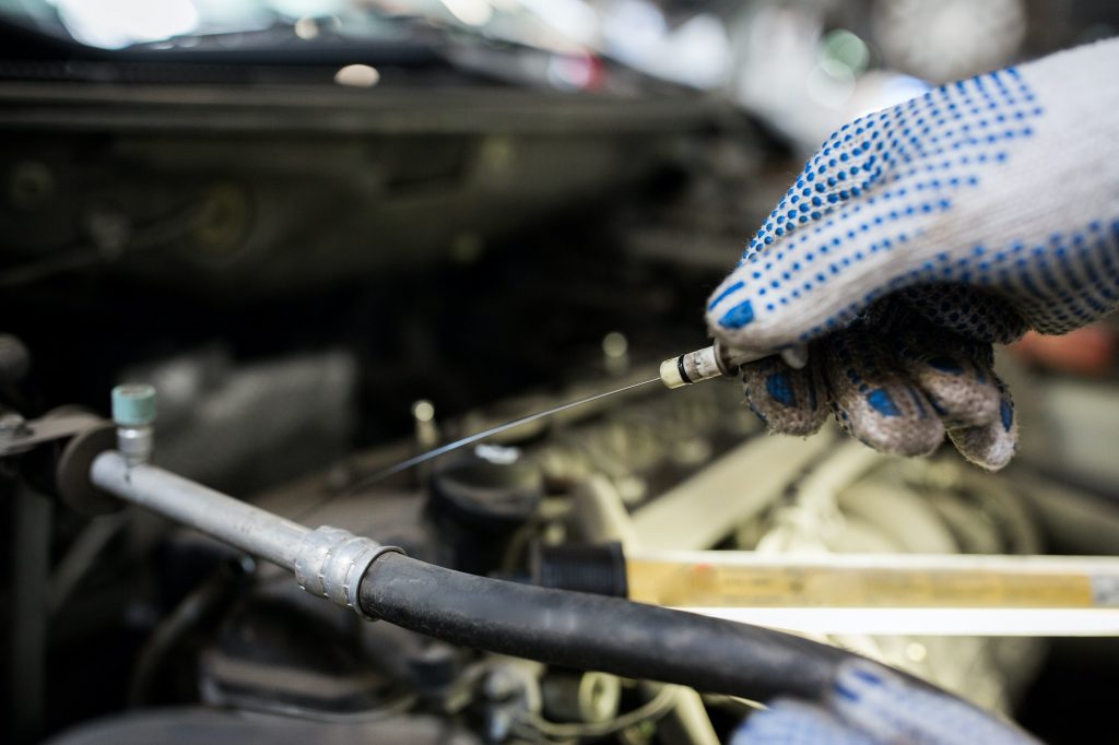 mechanic with dipstick checking motor oil level